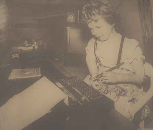 Picture of a young disabled woman using prosthetic arms to type on a typewriter.