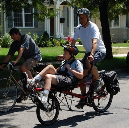 Man and younger disabled person bicycling on an adaptive bicycle.