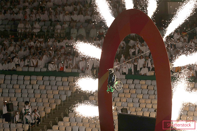 Picture of Aaron Fotheringham In the air on his wheelchair flying through a hoop with giant sparklers all around it 