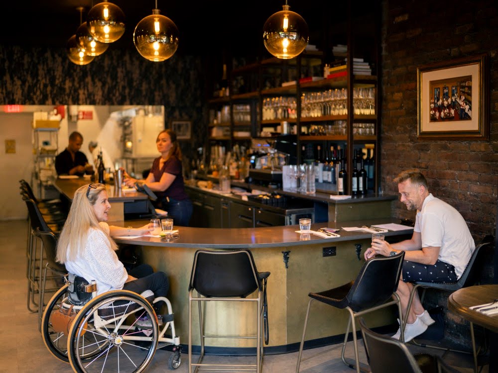 Woman in wheelchair sitting at a bar speaking to a man at the bar