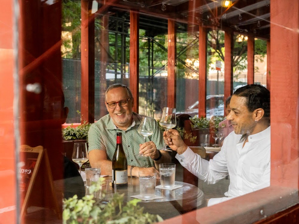 Arie Hochberg and George Gallego having a drink making a toast in the outdoor area 