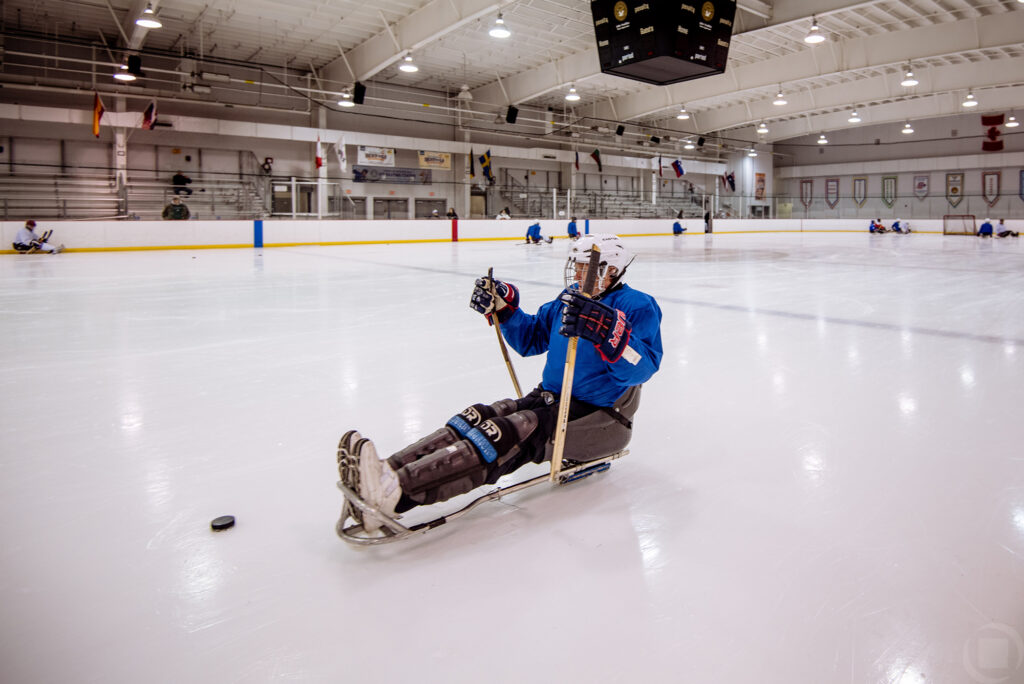 A disabled person at practice playing hockey using a sledge wearing a blue jersey.