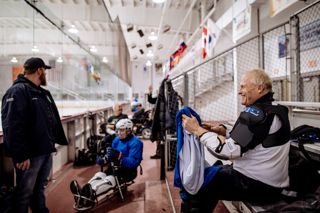 Man on bench putting on blue jersey getting ready to play hockey.