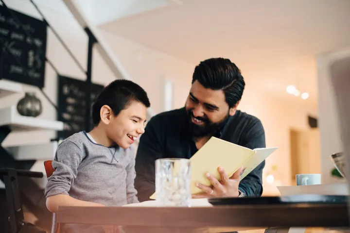 Picture of a young boy reading a book with his father.