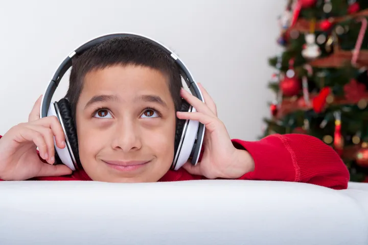 Picture of a young boy with headphones on smiling and looking up.