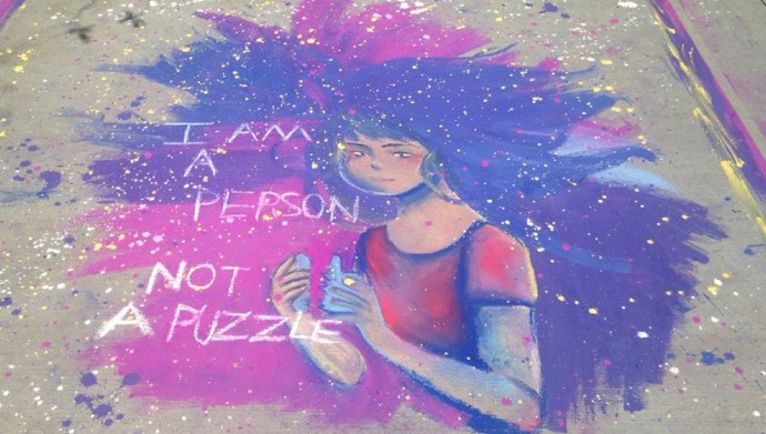 A chalk art drawing of a women with blue and purple hair that says "I am a person, not a puzzle".