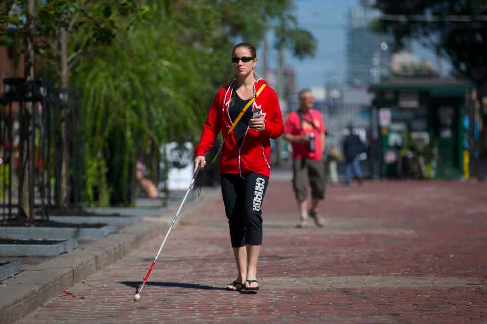 Picture of a woman walking down the street using her white cane.