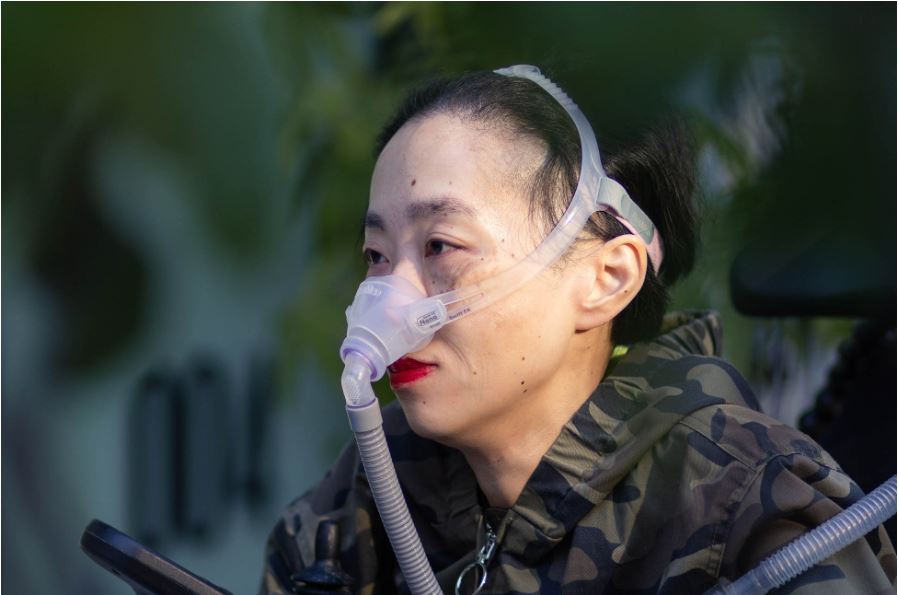 Picture of Alice Wong wearing an oxygen mask.