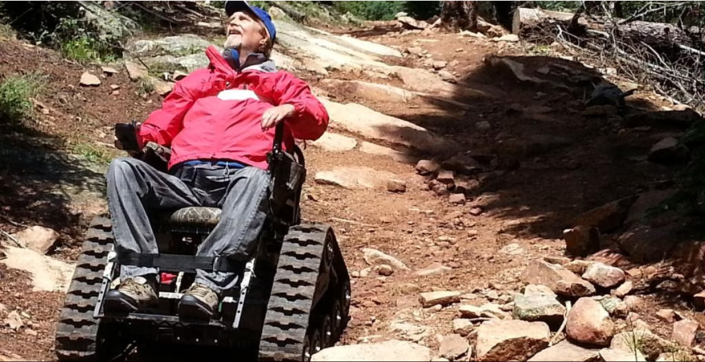 Picture of an elder man in a wheelchair that has track wheels.