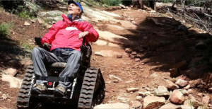 Picture of an elder man in a wheelchair that has track wheels.