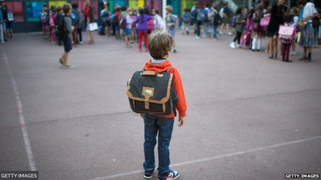 Image of a kid with his backpack on. His back is to the camera.