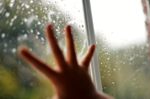 Picture of a kids hand on a window that has raindrops on it.
