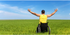 Picture of a man in his wheelchair in a field with his arms up in the air.