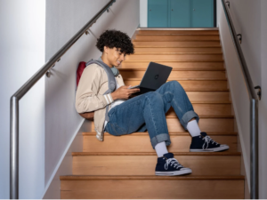 Picture of a teenage boy sitting on a set of stairs using a laptop.