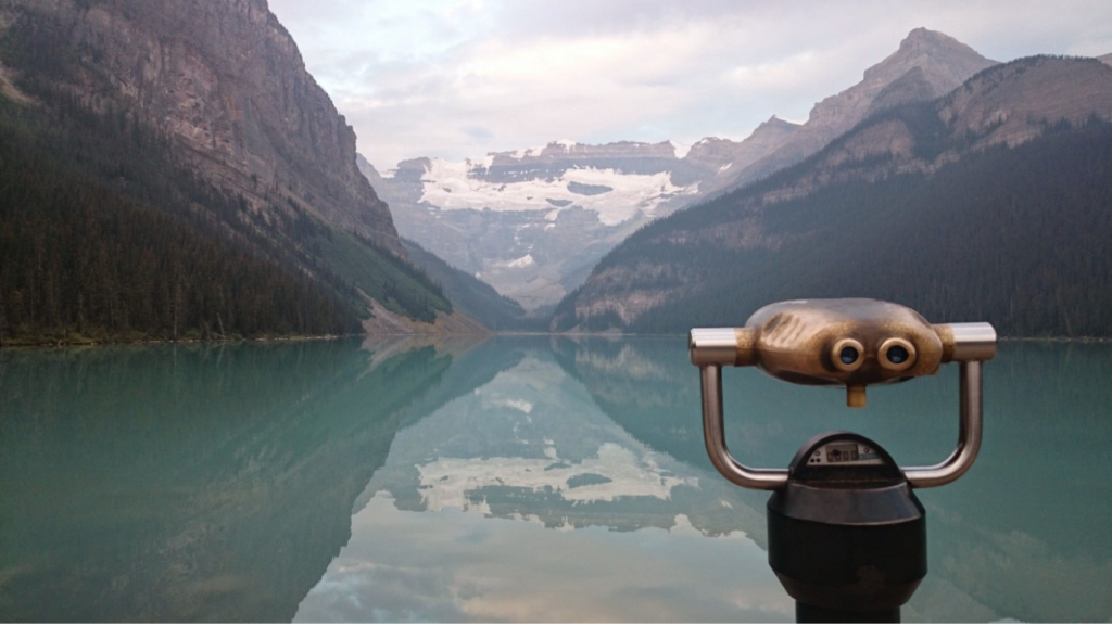 Image of a tower viewer in front of a big blue lake with mountains in the background.