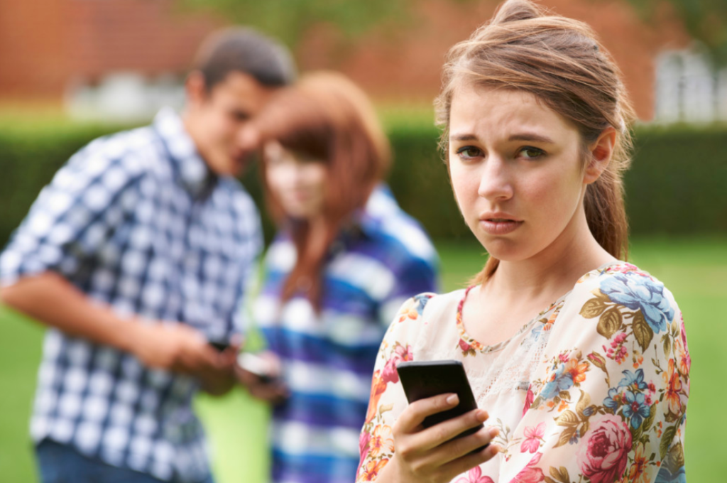 Image of two teenagers in background cyber bullying another teenager.