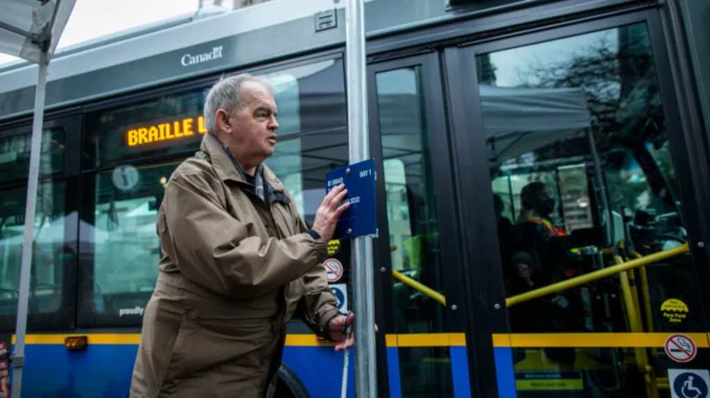 Image of a blind man feeling a braille sign at a bus stop.