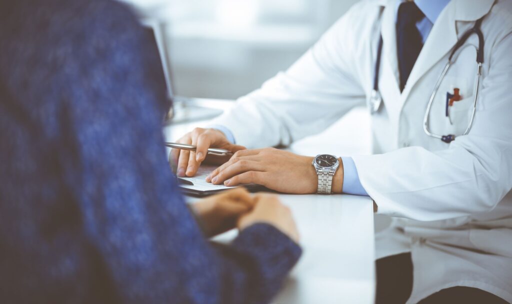 Doctor and patient at a table during a consultation. Only their torso and hands are visible.