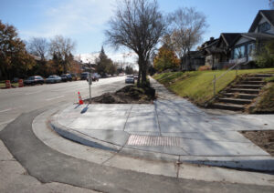 An urban neighbourhood street corner in the spring with the focus being a recently constructed curb cut sidewalk corner.