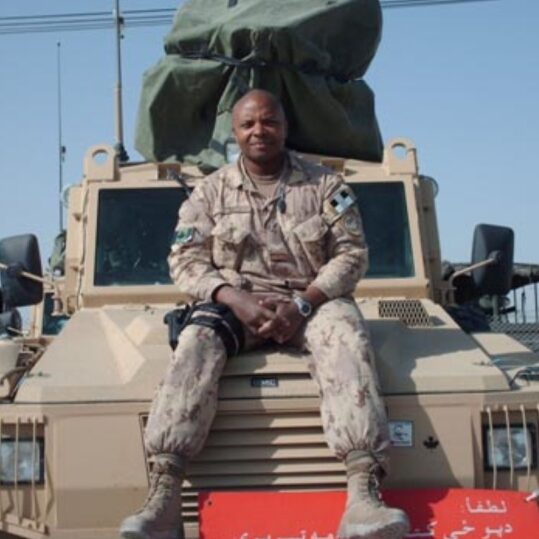 Mike Akpata in combat clothes on the hood of a military vehicle