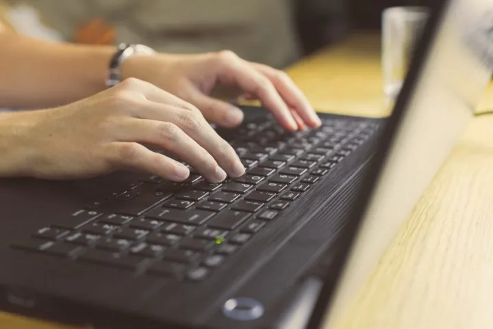 Zoomed in image of a persons hands  typing on a laptop.