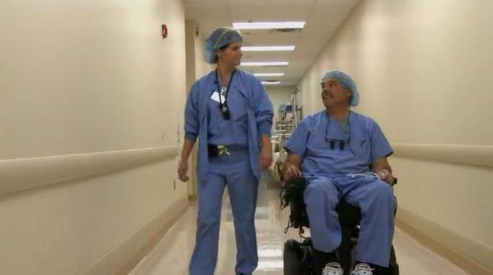 Dr. Rummel in wheelchair passing down a hallway with a colleague.