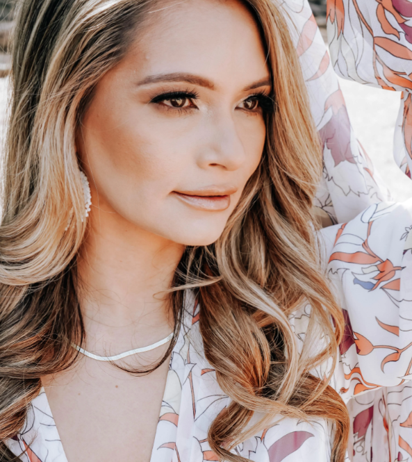 A close-up of Marcela Marañon wearing earrings, a necklace, and a white and purple blouse gazing to the right.