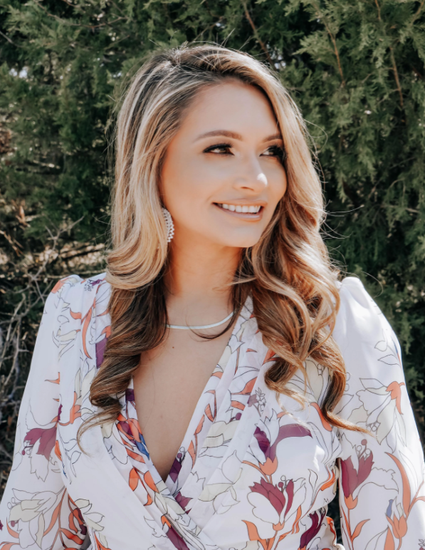 A portrait of Marcela in front of greenery.