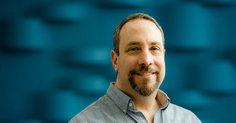 A portrait of Devin smiling in front of a blue background.